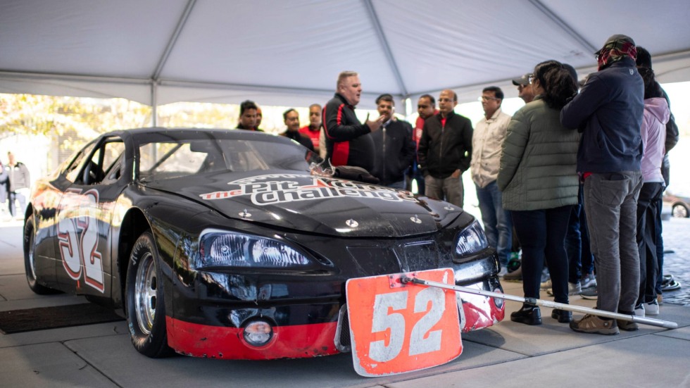 students standing around a race car listening to an instructor